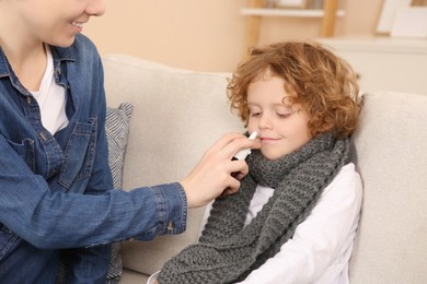 Mother using nasal spray to treat her little son on sofa indoors, closeup