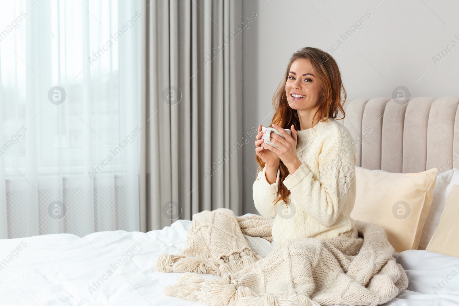 Photo of Happy beautiful woman with warm plaid and cup of drink in bed at home