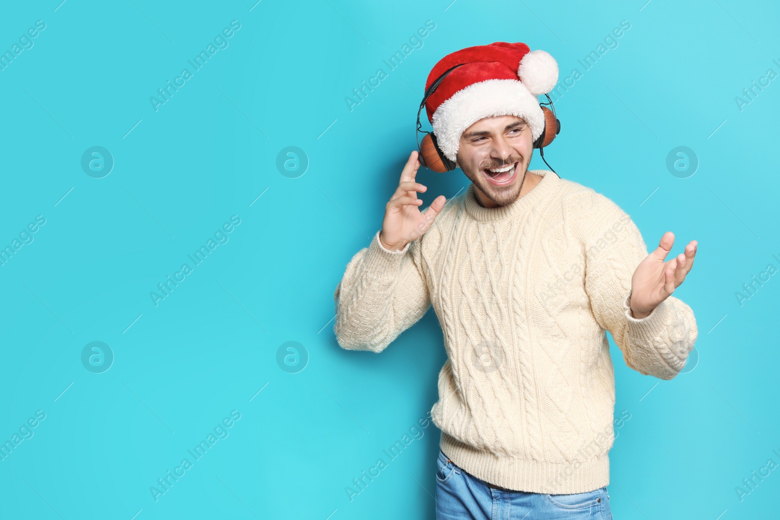 Photo of Young man in Santa hat listening to Christmas music on color background