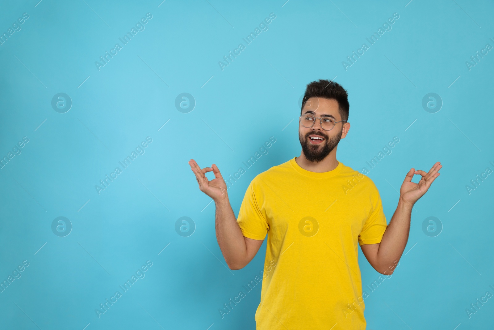 Photo of Young man meditating on light blue background, space for text. Zen concept