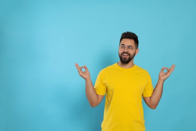 Photo of Young man meditating on light blue background, space for text. Zen concept