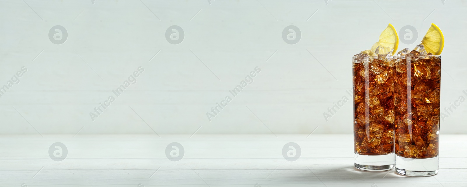 Image of Tasty refreshing soda drink with ice cubes and lemon slices on white wooden table. Banner design with space for text