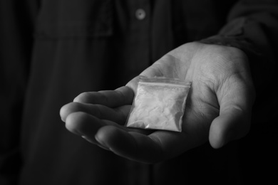 Photo of Drug dealer holding bag with cocaine, closeup. Black and white effect