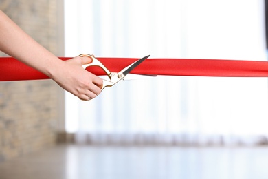 Photo of Woman cutting red ribbon on blurred background