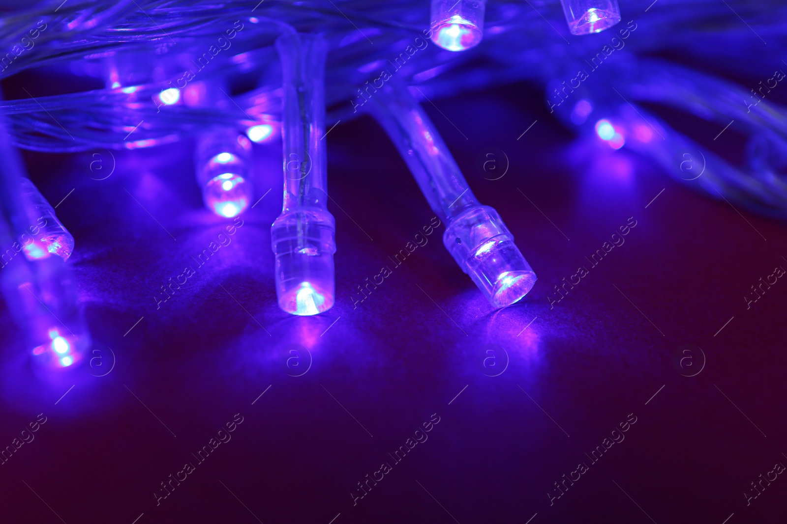 Photo of Glowing Christmas lights on dark red background, closeup