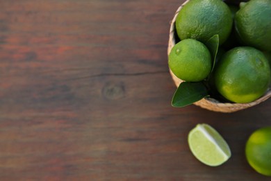 Fresh ripe limes and wicker basket on wooden table, flat lay. Space for text