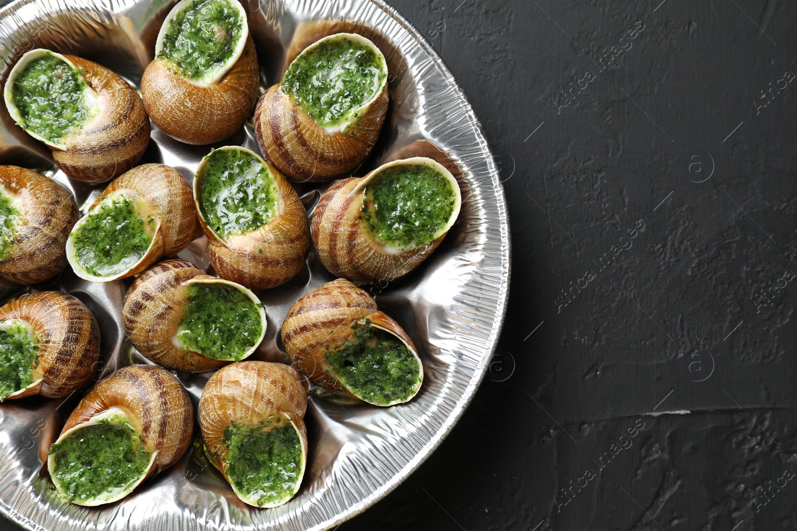 Photo of Delicious cooked snails on dark textured table, top view. Space for text