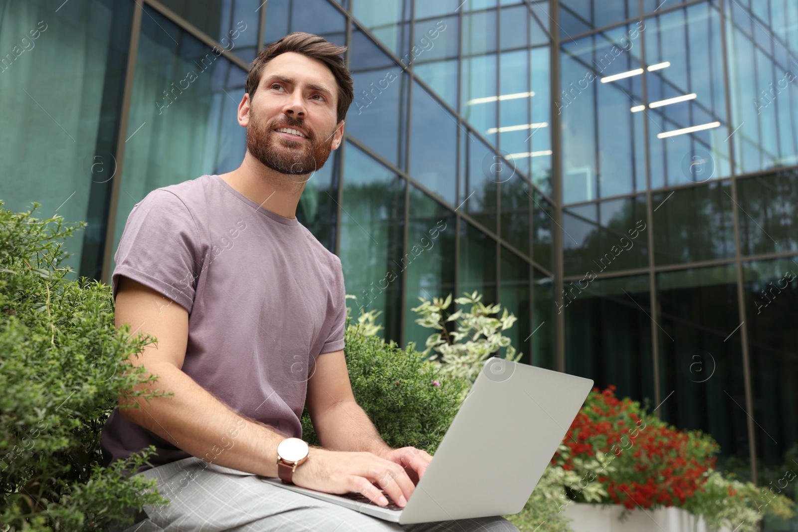 Photo of Handsome man with laptop near beautiful plants on city street