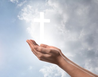 Image of Religion. Christian woman praying against sky with glowing cross, closeup