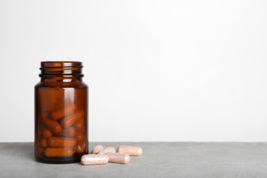 Gelatin capsules and bottle on light grey table against white background, space for text