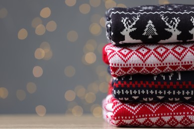 Photo of Stack of different Christmas sweaters on table against grey background with blurred lights. Space for text