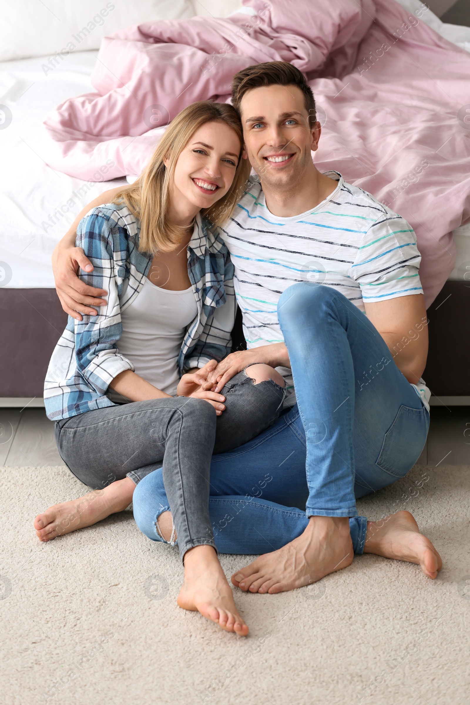 Photo of Lovely young couple sitting near bed on cozy carpet at home