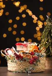 Photo of Wicker basket with Christmas gift set on wooden table against blurred festive lights. Space for text