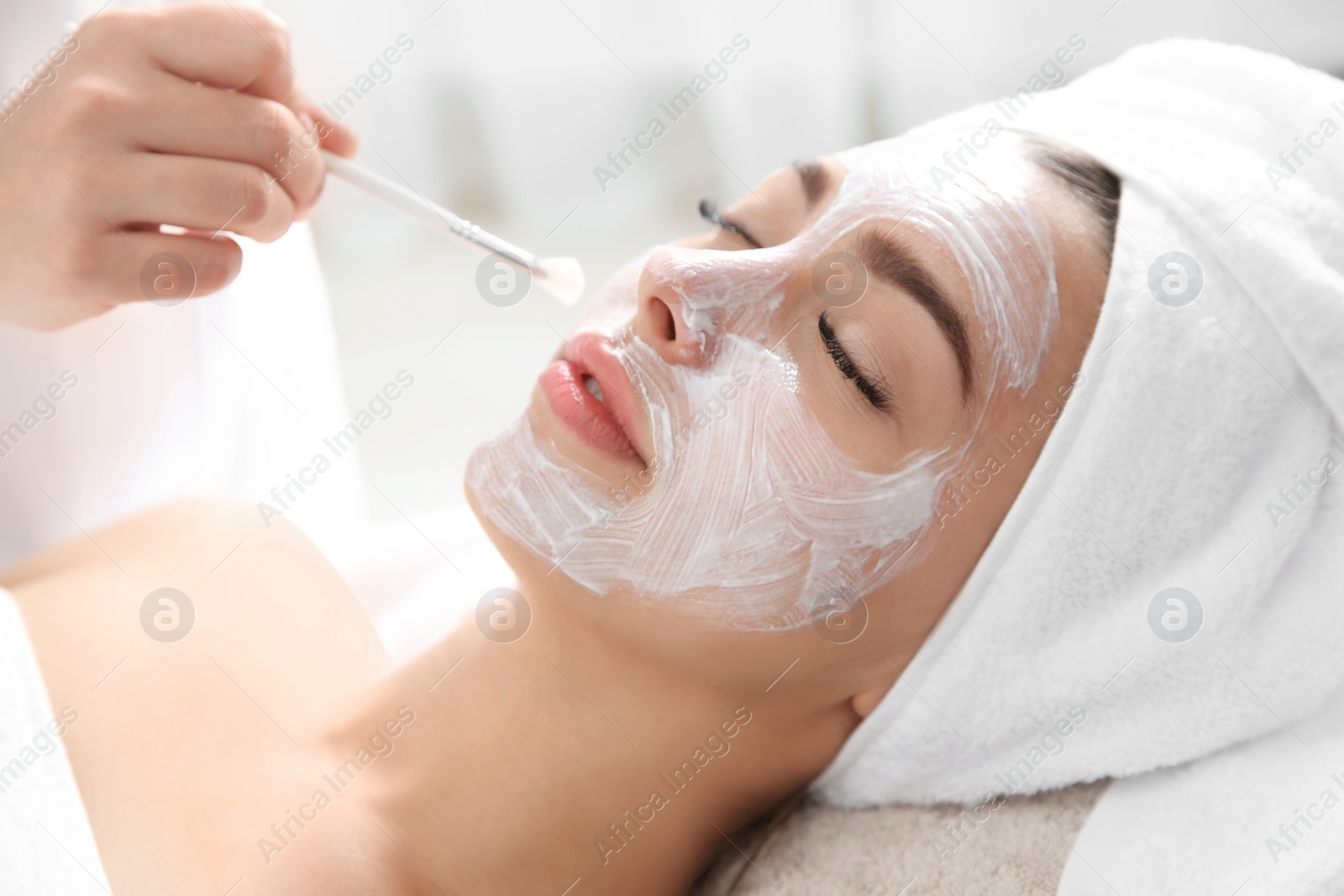 Photo of Cosmetologist applying mask on client's face in spa salon