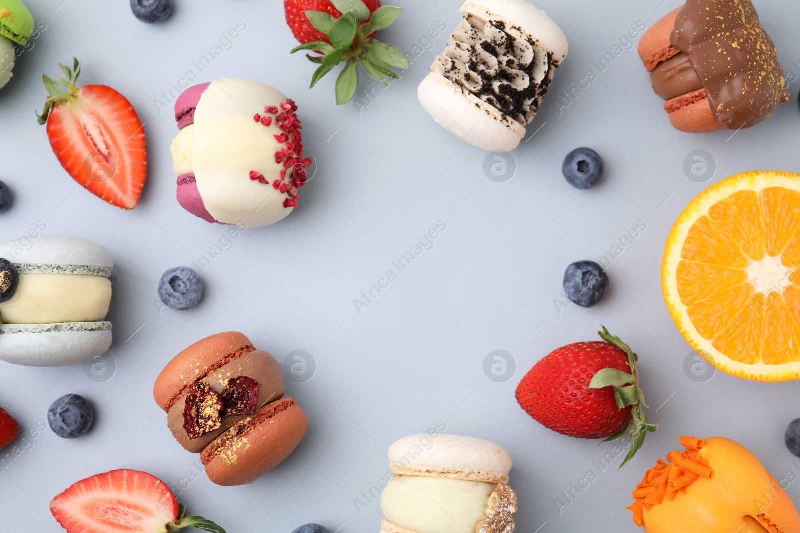 Photo of Frame made of delicious macarons, orange and berries on light blue table, flat lay. Space for text