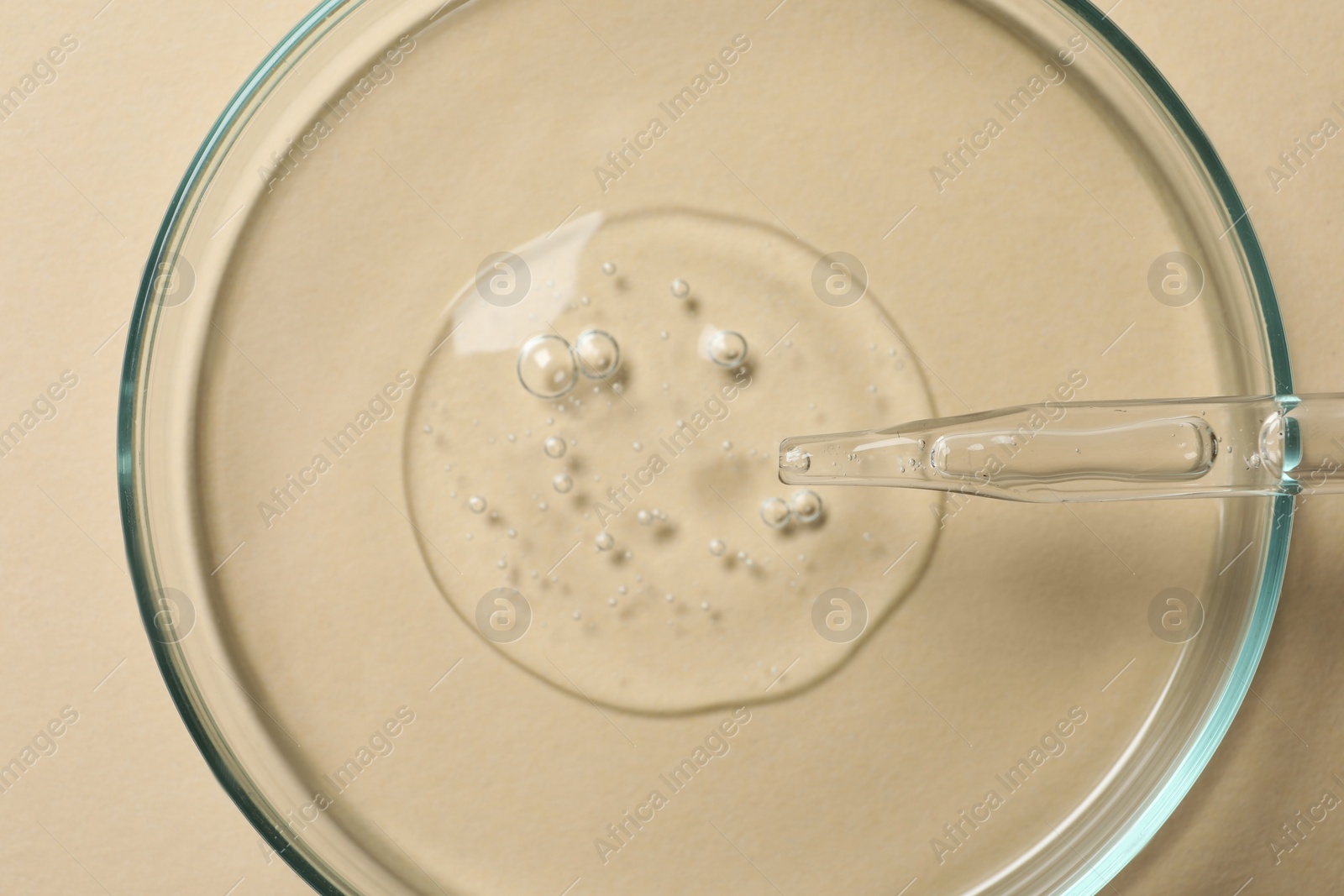 Photo of Petri dish with sample of cosmetic oil on beige background, top view