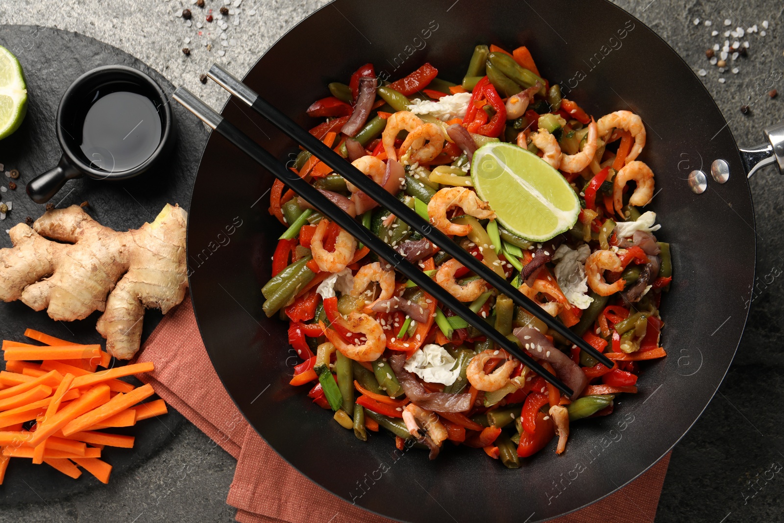 Photo of Shrimp stir fry with vegetables in wok and chopsticks on grey table, flat lay