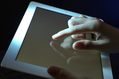 Woman using tablet on dark background, closeup