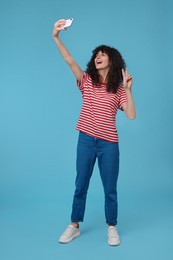 Beautiful young woman taking selfie on light blue background