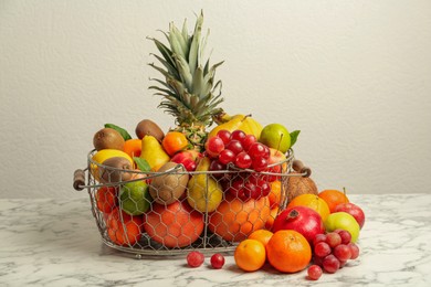 Metal basket with different fresh fruits on white marble table