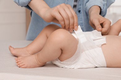 Photo of Mother changing baby's diaper on bed at home, closeup