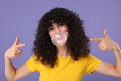 Beautiful young woman blowing bubble gum on purple background