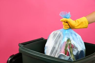 Woman throwing garbage bag into bin on pink background, closeup