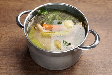 Pot with tasty bouillon on wooden table