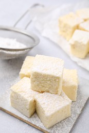 Delicious sweet marshmallows with powdered sugar on light grey table