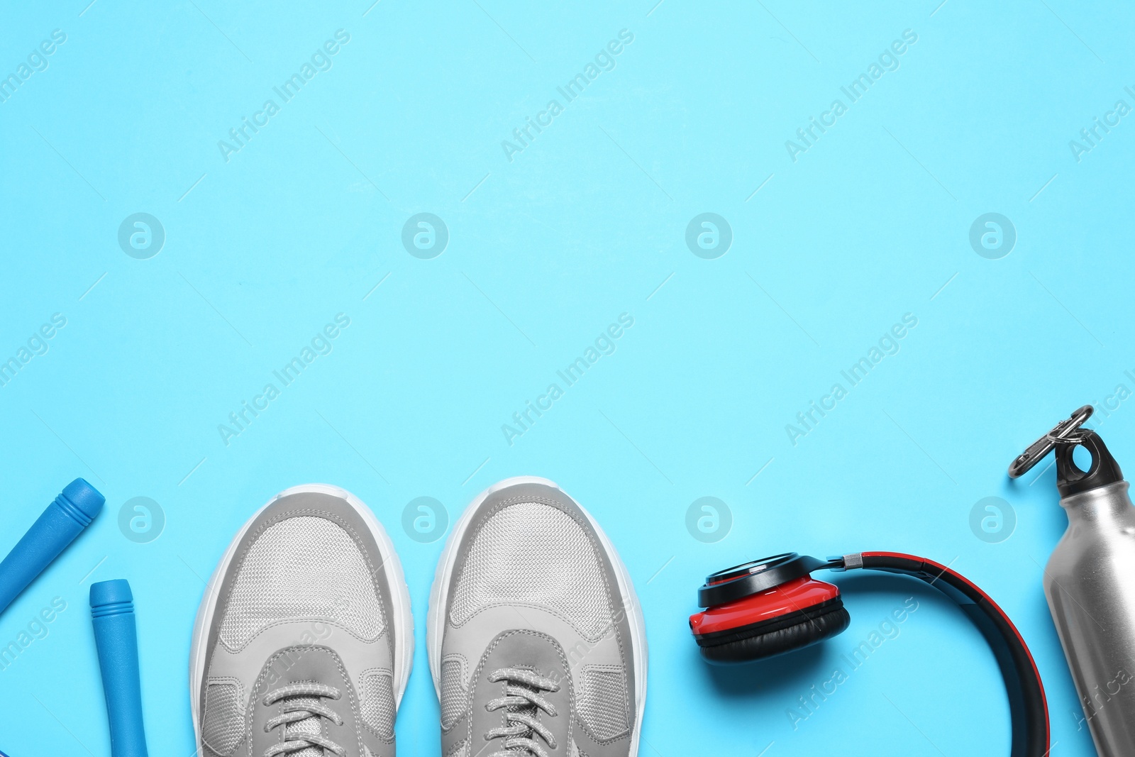 Photo of Flat lay composition with man's sneakers and fitness items on light blue background, space for text