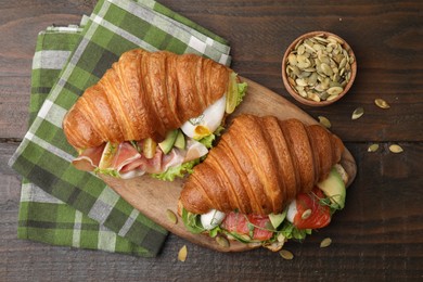 Photo of Delicious croissants with salmon, prosciutto and pumpkin seeds on wooden table, flat lay