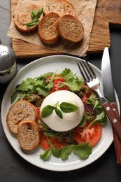 Photo of Delicious burrata salad with tomatoes, arugula and pesto sauce served on black table, flat lay