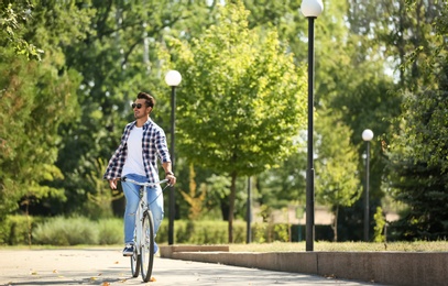 Photo of Handsome young hipster man riding bicycle in park