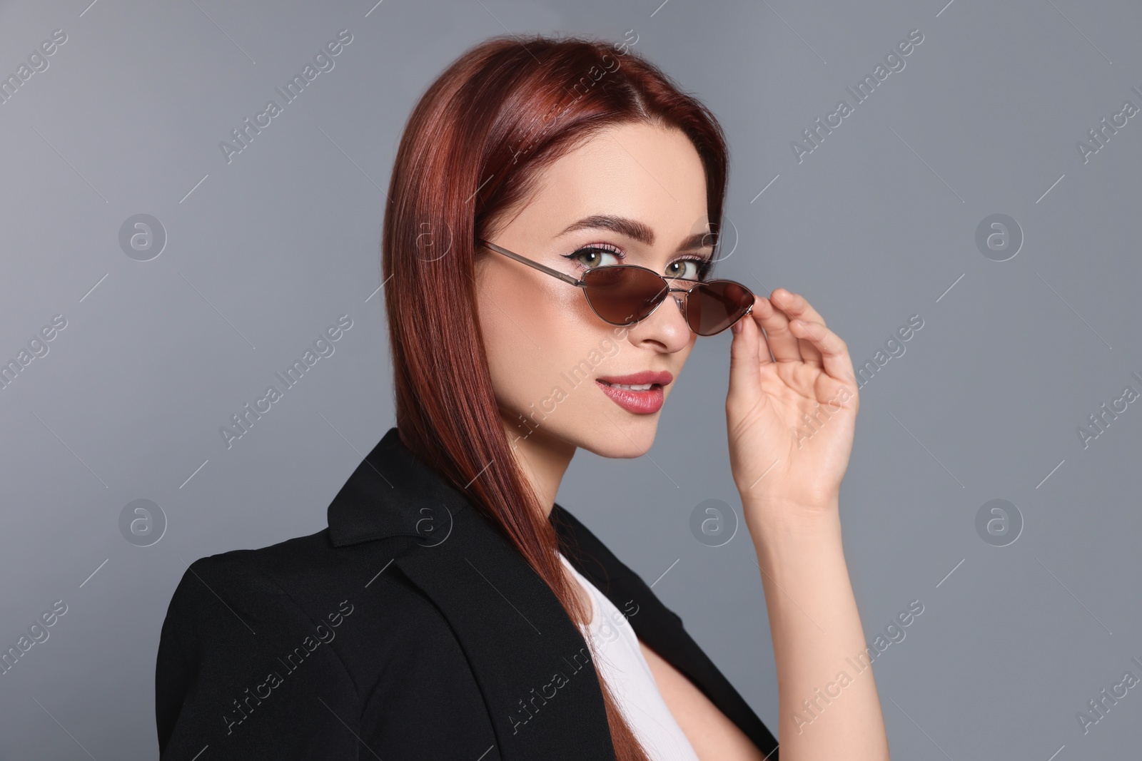 Photo of Stylish woman with red dyed hair and sunglasses on light gray background