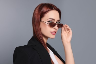 Stylish woman with red dyed hair and sunglasses on light gray background