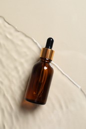 Photo of Bottle of cosmetic oil in water on beige background, top view.