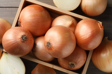 Whole and cut onions on wooden table, flat lay