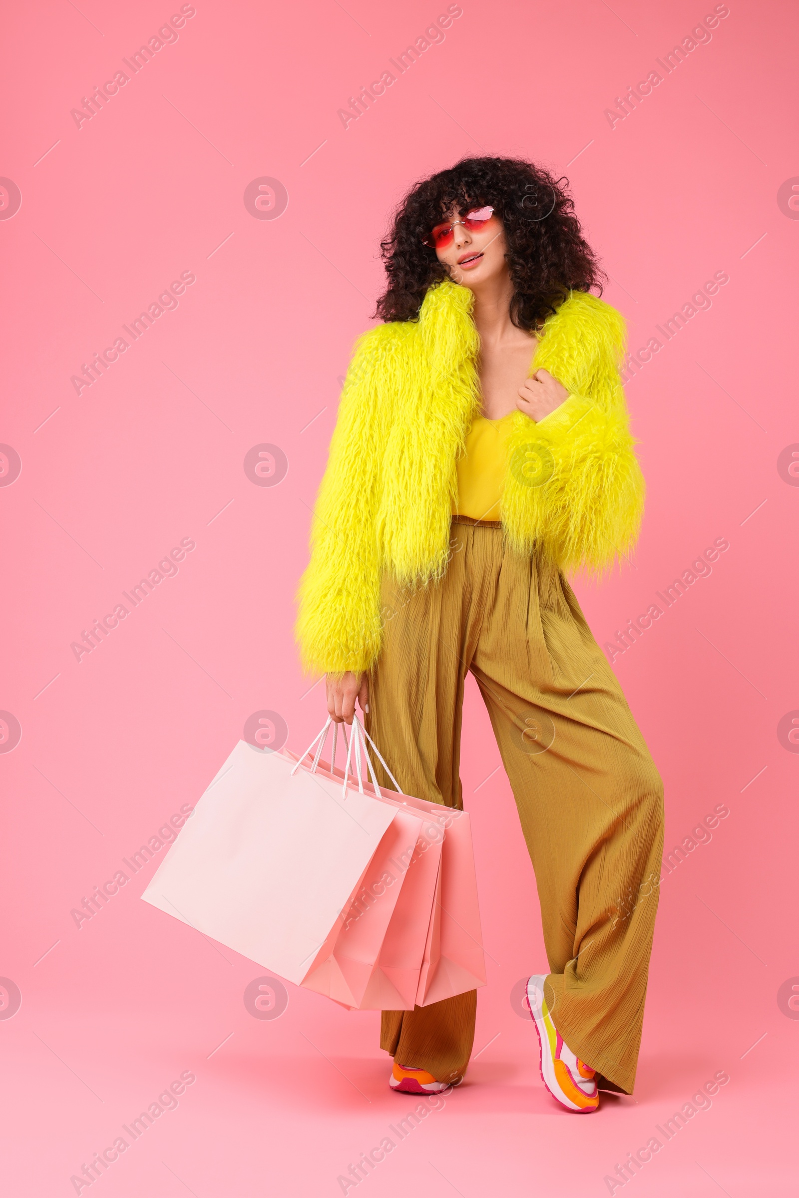 Photo of Happy young woman with shopping bags on pink background