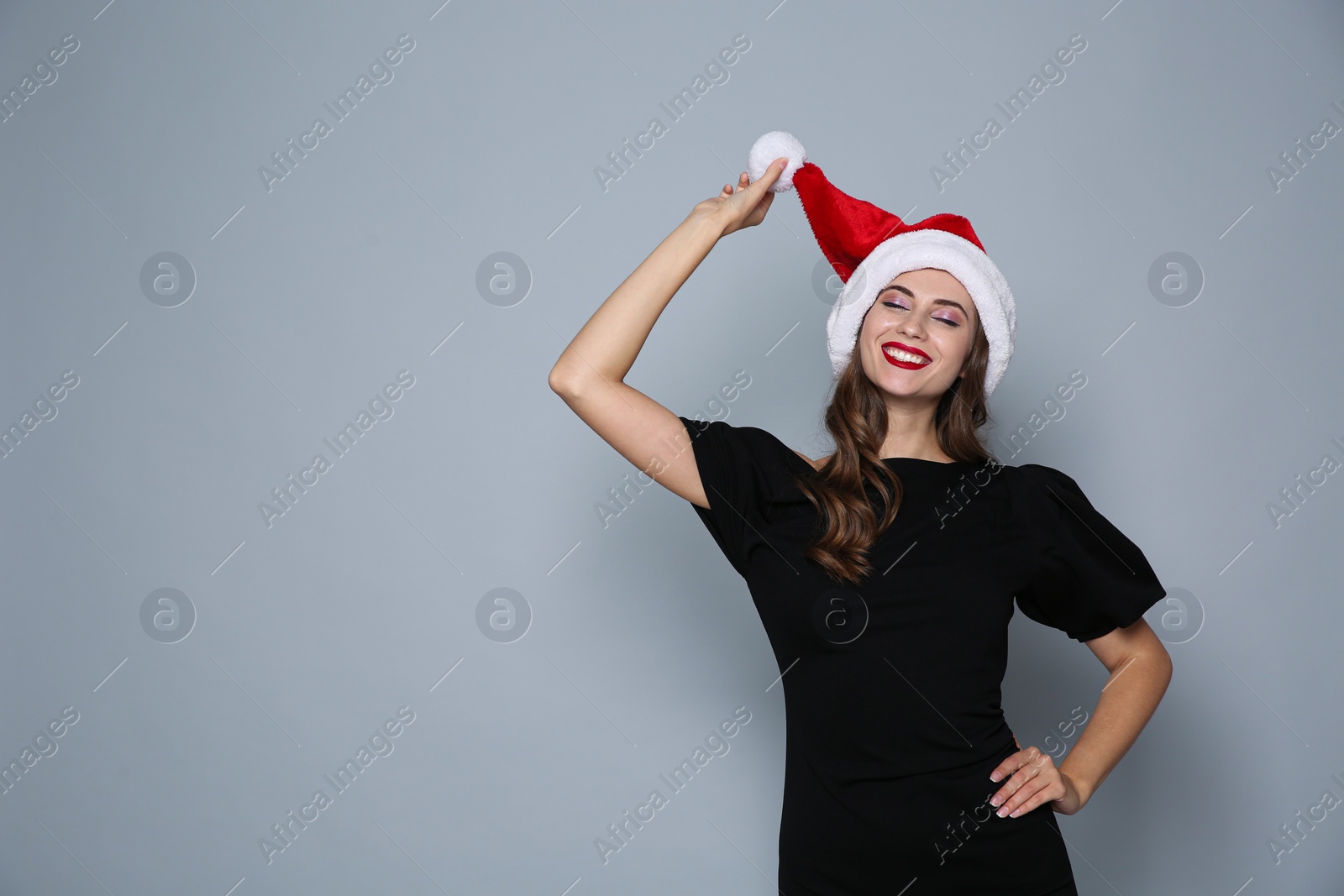 Photo of Happy woman in Santa hat on grey background, space for text. Christmas party