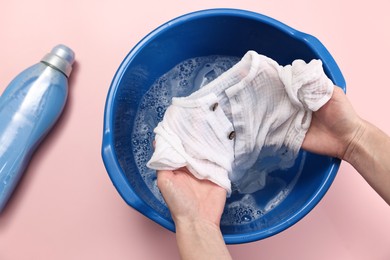 Woman washing baby clothes in basin on pink background, top view