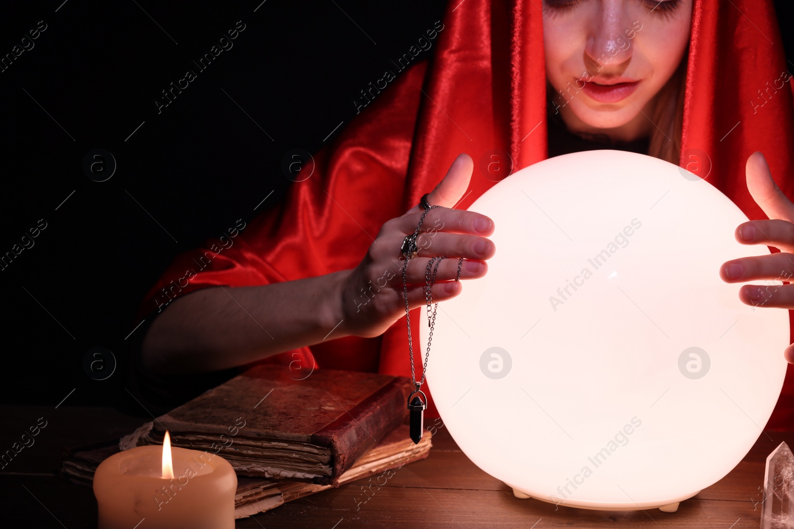 Photo of Soothsayer using glowing crystal ball to predict future at table in darkness. Fortune telling