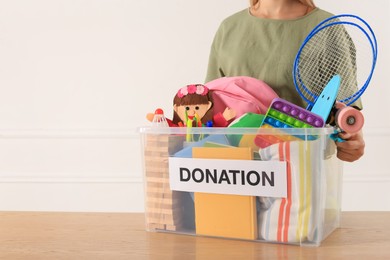 Photo of Woman holding donation box with child goods against light background, closeup. Space for text