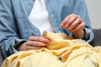 Photo of Woman sewing button with needle and thread onto shirt at home, closeup