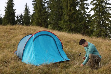 Man setting up blue camping tent on hill