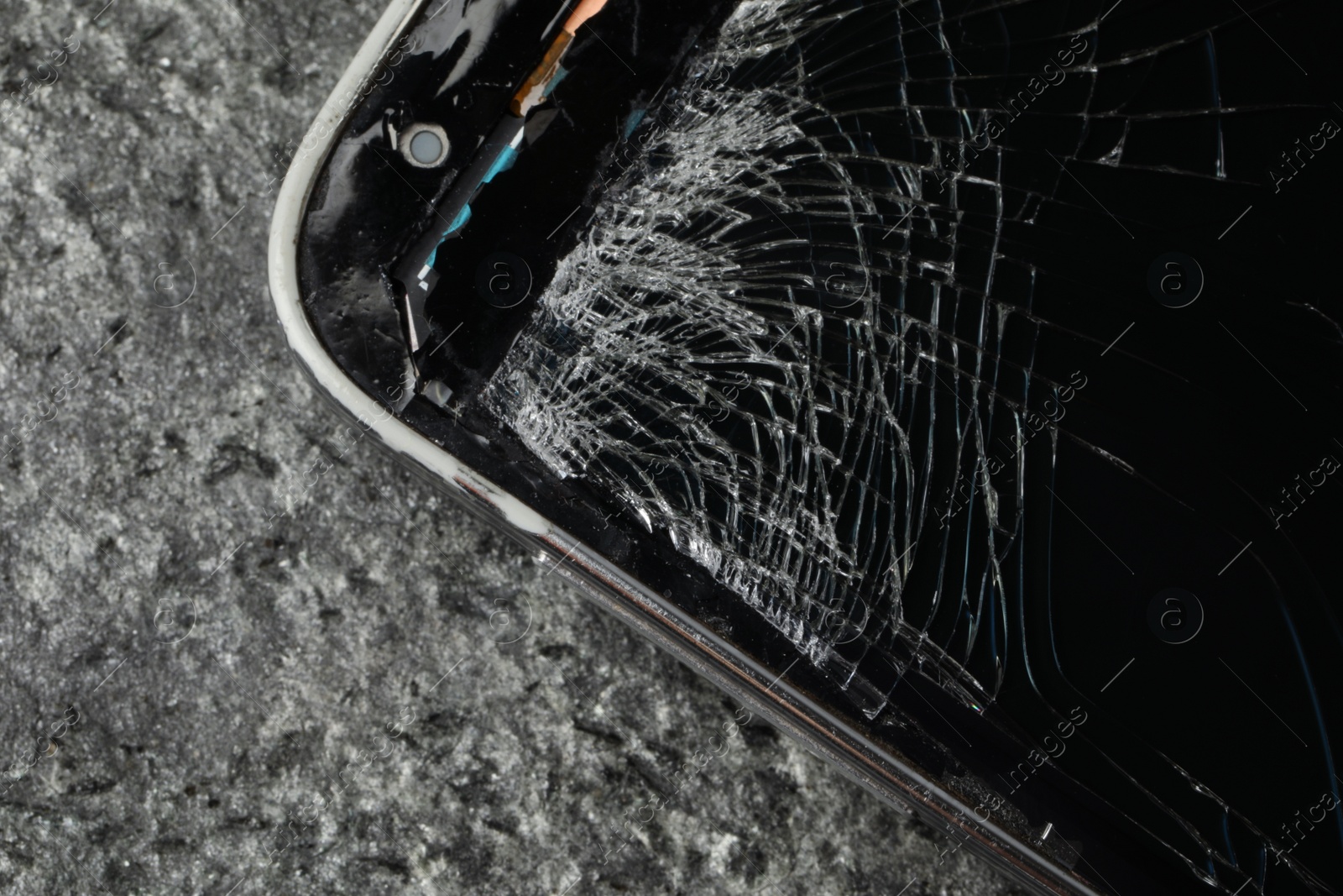 Photo of Smartphone with cracked screen on grey stone background, closeup. Device repair