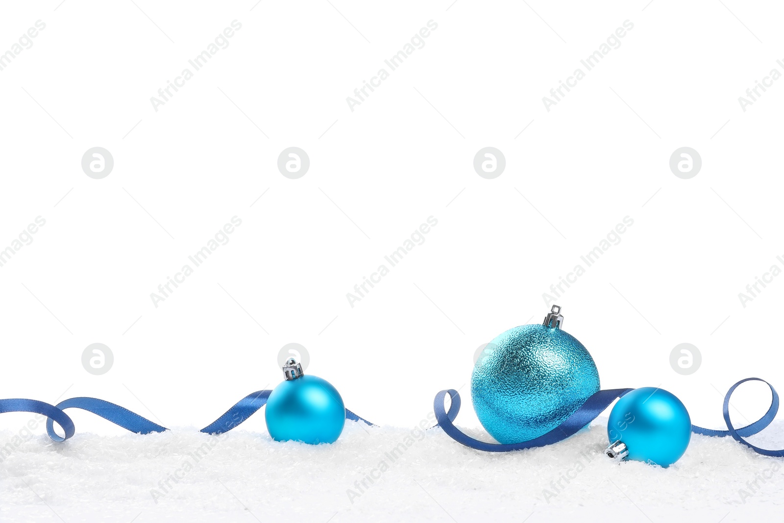 Photo of Beautiful light blue Christmas balls and ribbon on snow against white background