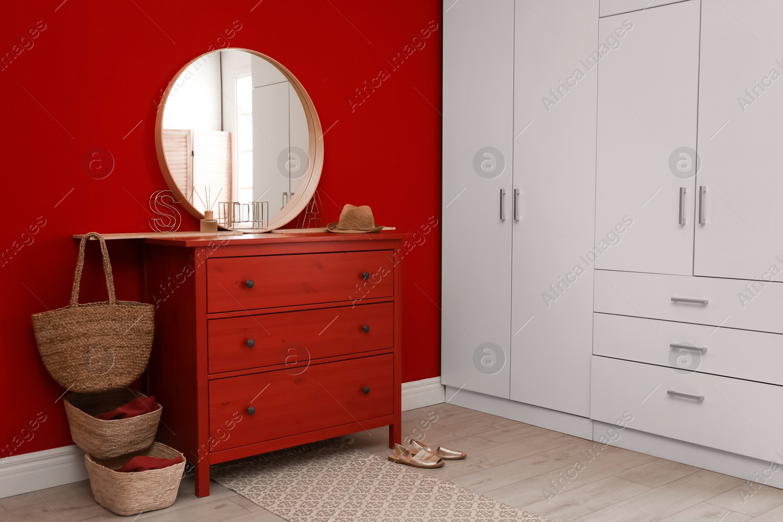 Photo of Round mirror and chest of drawers near red wall in room. Modern interior design