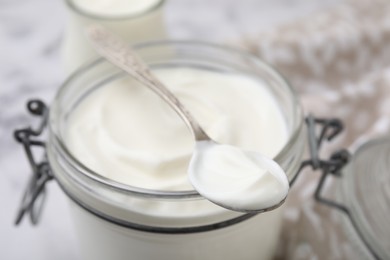 Photo of Delicious natural yogurt in glass jar and spoon on table, closeup