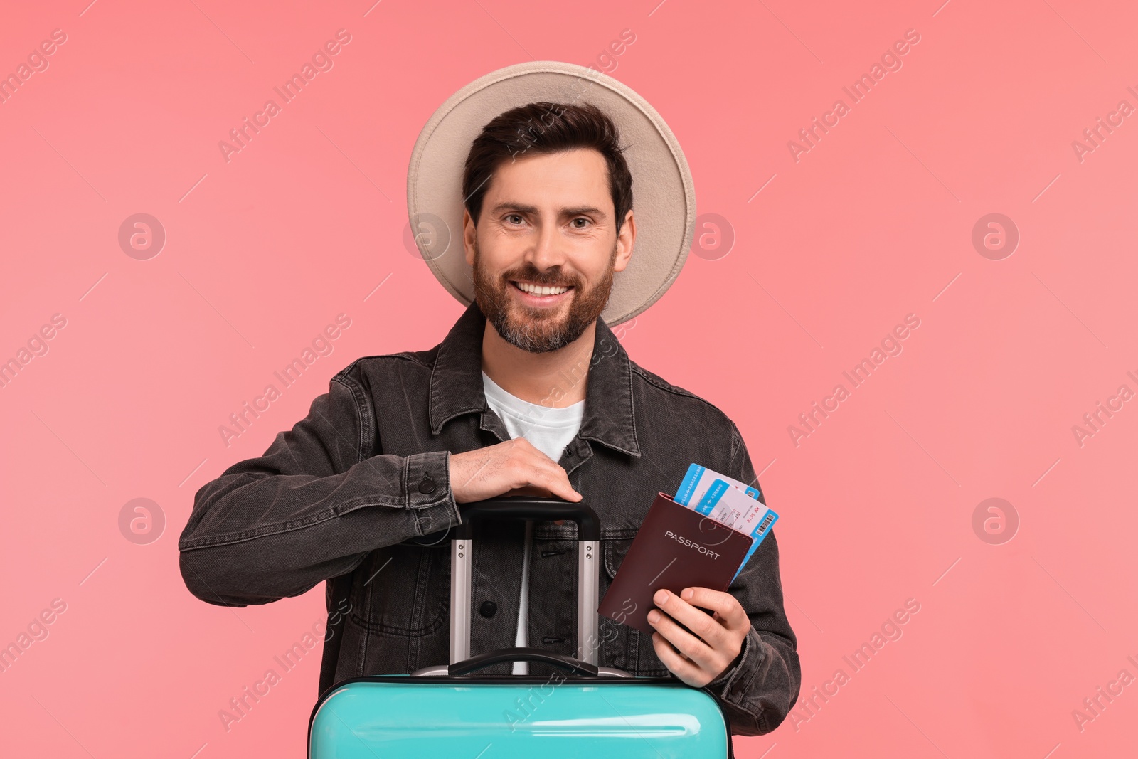 Photo of Smiling man with passport, tickets and suitcase on pink background