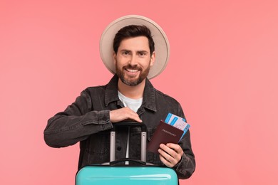 Smiling man with passport, tickets and suitcase on pink background